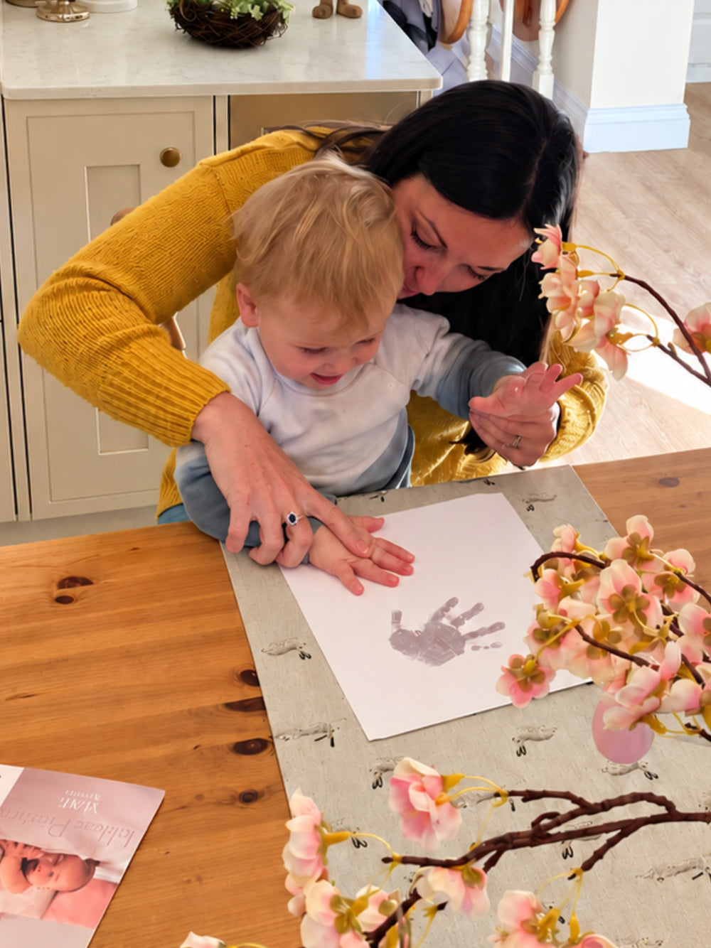Mother gently helping her toddler take a handprint at home using a baby handprint kit.